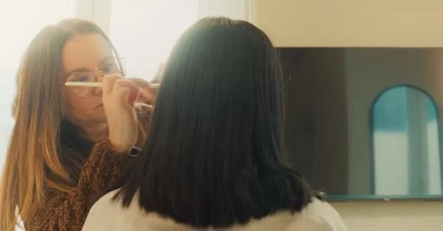 A makeup artist working with a woman in warm window light